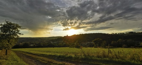 A rural scene with meadows and dirt roads at sunset, dramatic cloud formations, Franconian Forest nature park Park