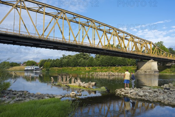 Yellow metal bridge across river with two anglers on the shore and blue sky, bridge over Morava river, Cuprija, Cuprija, Pomoravlje district, Serbia Europe