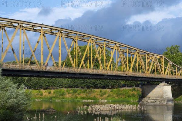 Yellow metal bridge over a river with green vegetation on the banks and cloudy sky, bridge over the Morava river, Cuprija, Cuprija, Pomoravlje district, Serbia Europe