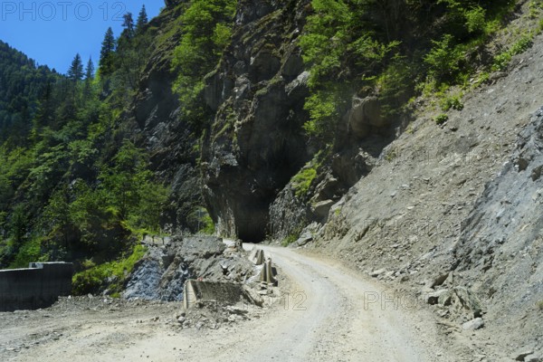 Gravel road winds around rocky mountain walls near a tunnel, road 7 partly slipped down, west of Mestia, Mingrelia region and Upper Svaneti, High Caucasus, Georgia