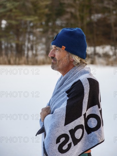 Man with cap, 55, standing on the ice wrapped in a towel after ice bathing, Thumsee, Bad Reichenhall, Berchtesgadener Land, Upper Bavaria, Bavaria, Germany