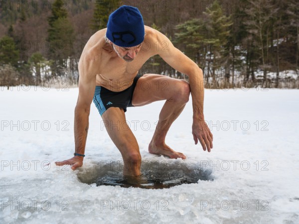Man with cap, 55, climbs into an ice hole for ice bathing, Thumsee, Bad Reichenhall, Berchtesgadener Land, Upper Bavaria, Bavaria, Germany