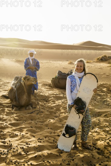 Young woman with snowboard in the sand dunes, near Merzouga, Meknès-Tafilalet region, Erg Chebbi, northern Sahara, Morocco