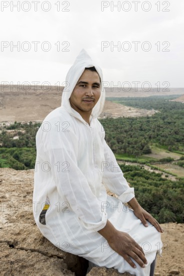 Young man and oasis in the background, near Merzouga, Meknès-Tafilalet region, Erg Chebbi, northern Sahara, Morocco