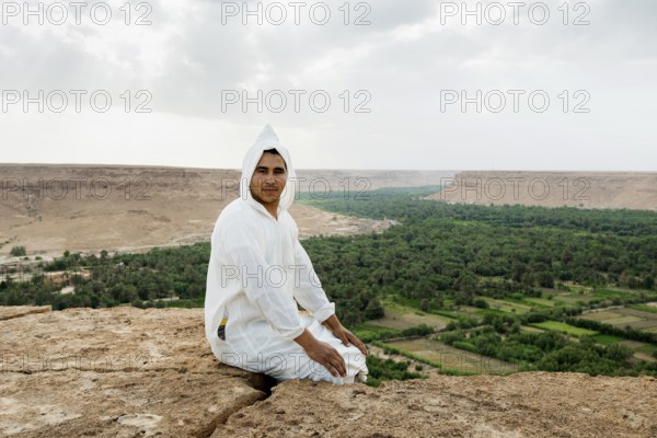 Young man and oasis in the background, near Merzouga, Meknès-Tafilalet region, Erg Chebbi, northern Sahara, Morocco