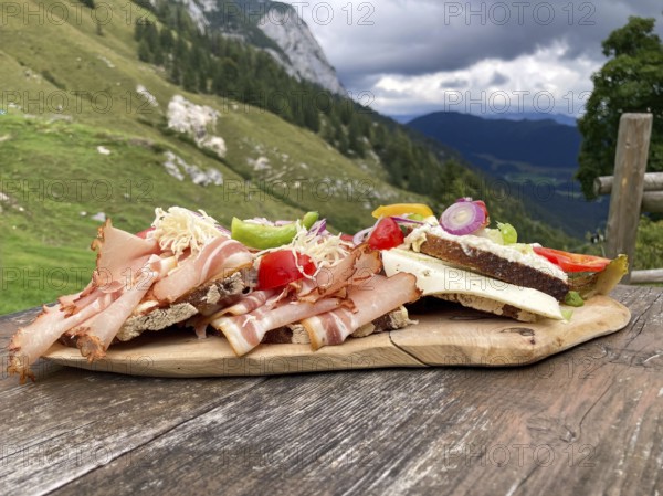 Typical snack on the alpine pasture, bacon bread and cheese bread on wooden plate on wooden table, Halsalm, Ramsau, Bavaria, Germany