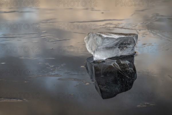 A piece of ice lies on the frozen surface of a lake in which clouds are reflected, Finland