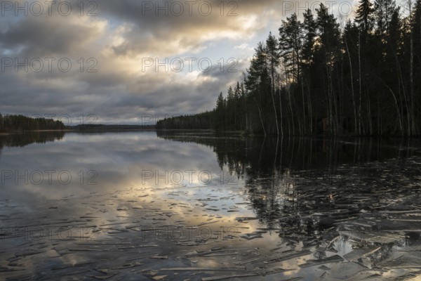 Pieces of ice and clouds reflecting on the water surface, lake in a forest, winter, Finland