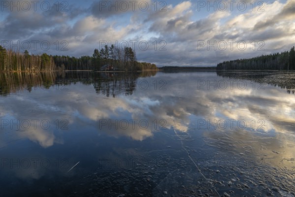 Ice and clouds reflecting on the water surface, lake in a forest, Finland