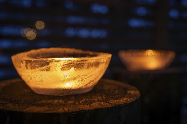 Ice bowls illuminated by burning tea lights stand on tree trunks, winter, Finland