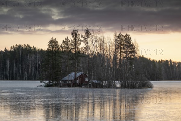 Small island with a red house, frozen lake in winter, edge of forest, near Hartola, Finland