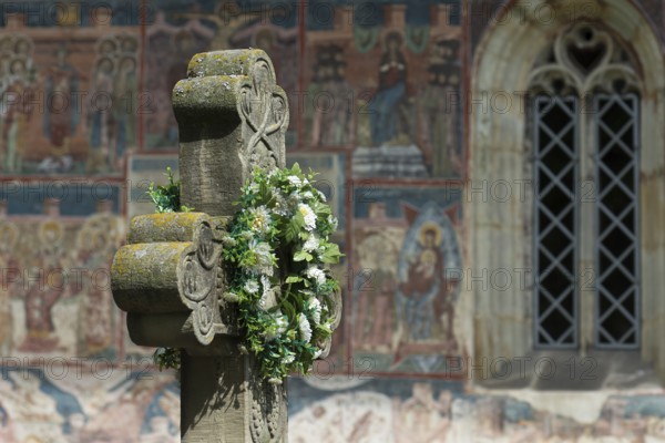 Artificial flower wreath on a stone cross in front of the Romanian Orthodox Women's Monastery, 1530, Gura Humorului, Romania