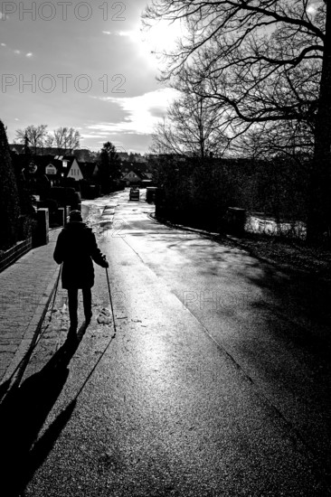 Aetere woman with sticks running on rain-wet road in backlight, black and white, Eckental, Middle Franconia, Bavaria, Germany
