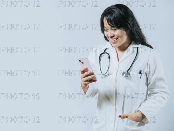 Smiling asian doctor using smartphone isolated. Young asian female doctor using phone, Female healthcare worker holding cellphone