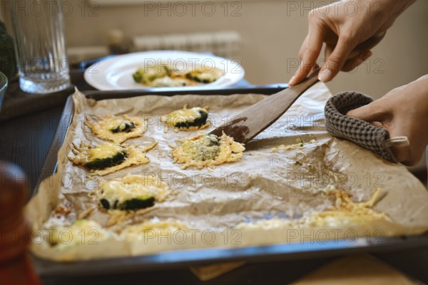 Unrecognizable woman transfers roasted smashed broccoli with cheese from baking sheet to plate using wooden spatula, close-up view
