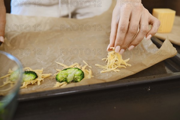 A person is placing shredded cheese on a baking sheet in a kitchen. The broccoli is ready to be baked. This process shows a simple cooking activity