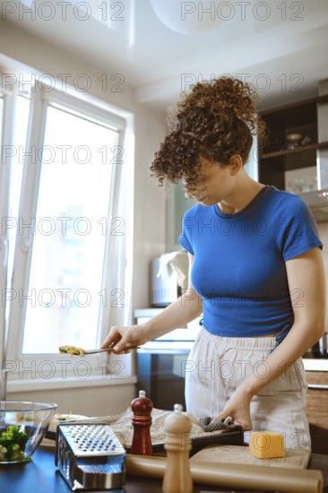 In a bright kitchen, a woman prepares smashed broccoli mixed with cheese. She stands at the counter, focused on her task. Fresh ingredients are nearby, ready for cooking