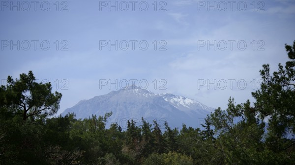 A snow-covered mountain above a wooded landscape under clear skies, view of Mount Tahtali, Lycia, Turkey