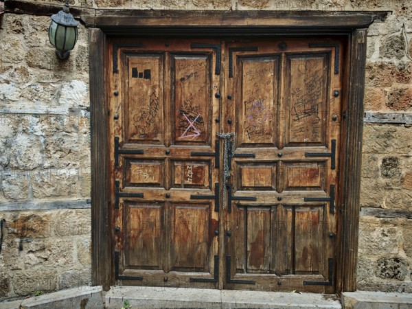 Old wooden door with graffiti on a stone wall, next to it an old lamp, Antalya Turkey