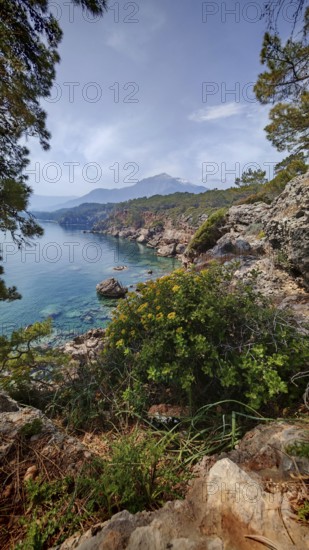 Rocky coastal landscape with clear water, lush vegetation and a Tahtali mountain in the background, Lycian Way, Turkey