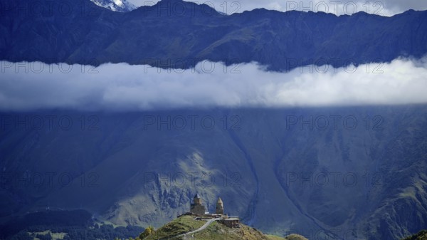Church on a hill below a massive mountain with a band of clouds, Gergeti Monastery, Georgia