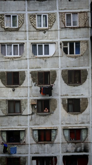 Dilapidated residential building with open windows and people in a simple environment, Tbilisi, Georgia