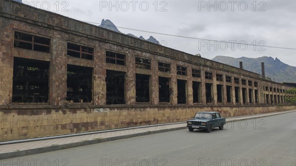 Abandoned large building and a car on a quiet road in the background mountains and clouds, Alaverdi, Armenia
