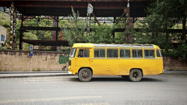 An old yellow bus is parked in front of an abandoned industrial plant in an urban area, Alaverdi, Armenia
