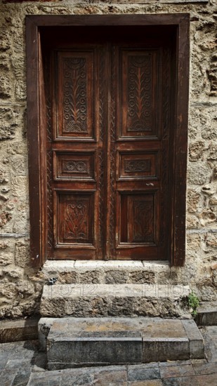 Decorated antique wooden door set into a rough stone wall, Antalya Turkey
