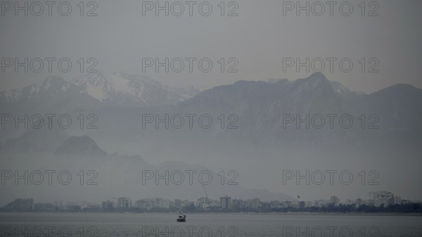 Foggy lake with a distant boat against a mountain backdrop, Antalya, Turkey