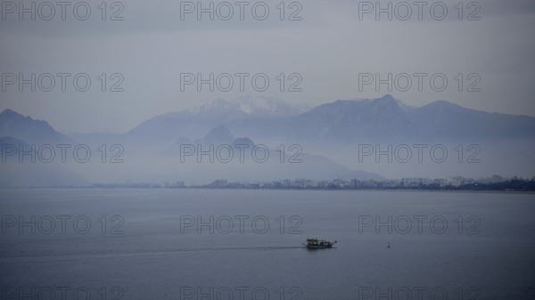 Single boat sails across foggy lake against mountain backdrop, Antalya, Turkey
