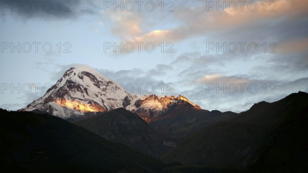 Sunset over snowy mountain with dramatic sky, Kazbek, Stepantsminda, Georgia