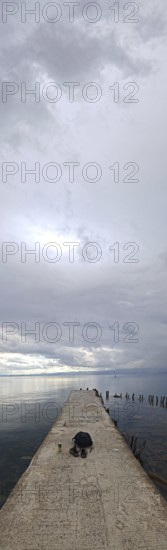 Long footbridge leading into a quiet lake surrounded by cloudy skies, Lake Ohrid, North Macedonia