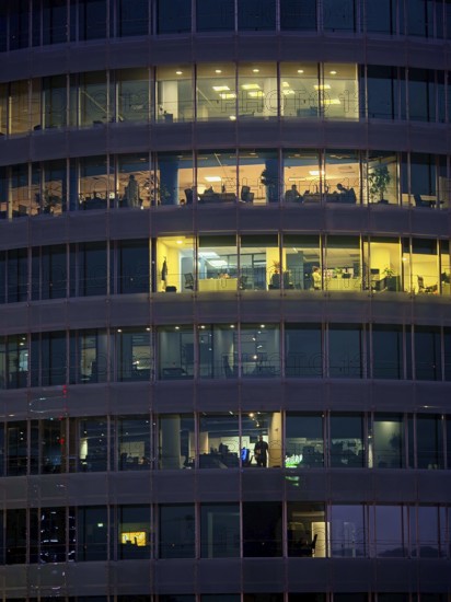 View of illuminated windows of an office building at night, people visible at work, Tirana, Albania
