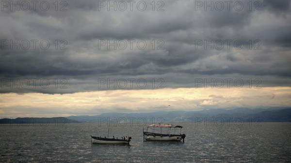 Boats on a still lake under a cloudy sky, peaceful scenery, Orhid Lake, North Macedonia