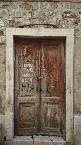Weathered wooden door with graffiti in an old stone wall, Slovenia