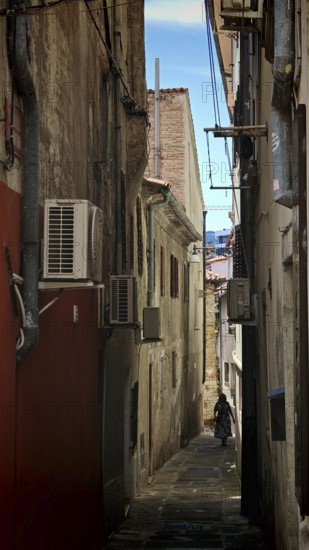 Narrow, shady alley with old buildings and visible air conditioners, Koper, Slovenia