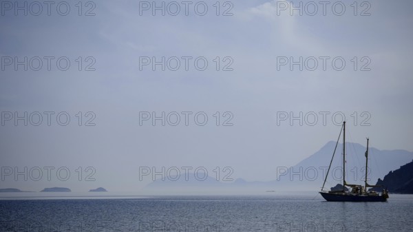 A sailboat in a foggy atmosphere on the sea with silhouetted mountains, Antalya, Turkey