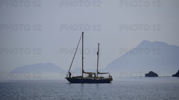 A lonely sailboat in the still sea with misty mountains in the background, Antalya, Turkey