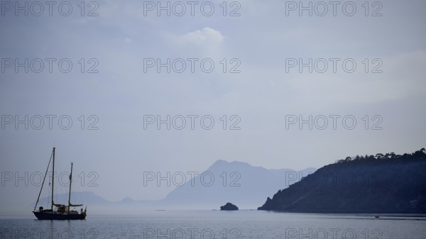 A sailboat in the misty sea with silhouetted mountains in the background, Antalya, Turkey