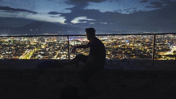 Person in front of illuminated cityscape at night, relaxed atmosphere, Prizren, Kosovo