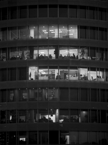 Black and white photo of an illuminated office building with visible floors and people, Tirana, Albania