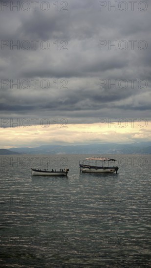 Two boats calm on a lake under a thick, cloudy sky, Orhid Lake, North Macedonia