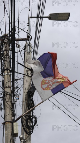 Serbian flag on a power pole blowing in the wind against a grey sky, Kosovo