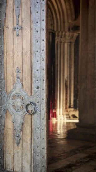 A massive wooden door with detailed metal ornaments opens to a Gothic interior, Kosovo