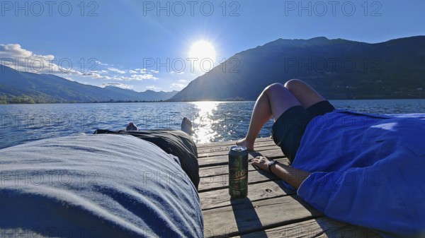 Two people relax on a jetty in front of an impressive mountain backdrop at the lake, Plav Lake, Montenegro