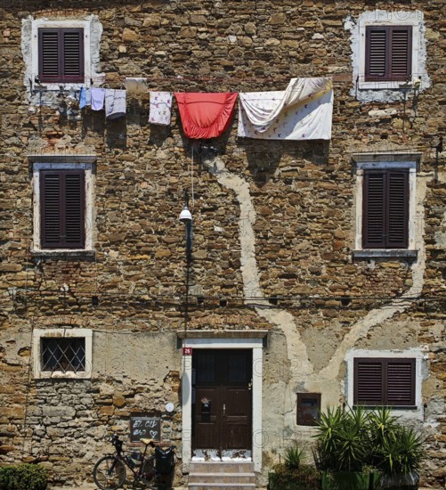 Rustic stone wall with hanging clothes and closed shutters, Koper, Slovenia