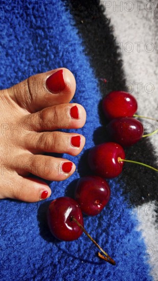 Red painted toes next to cherries on a colorful blanket