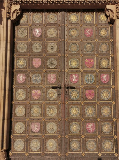 Large, richly decorated wooden door with golden and coloured coats of arms