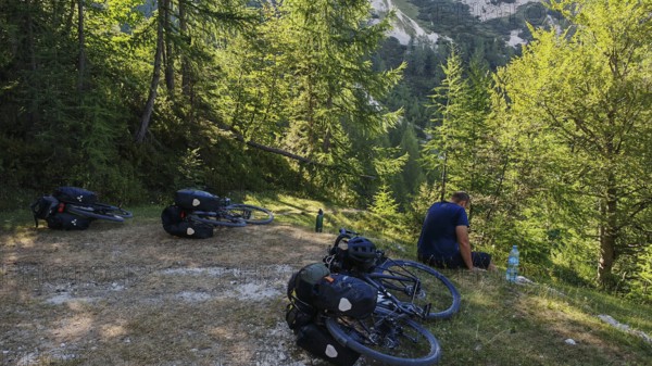 Person having a picnic in the woods with bicycles in a meadow surrounded by mountains
